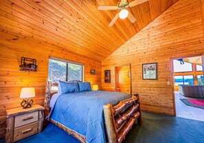 A log cabin bedroom with a bed, wooden walls, a ceiling fan, and a window. - Lakeview Lodge at Panguitch Lake (Panguitch)