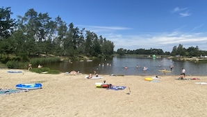 En strand med sandet bredde, en rolig sø og flere personer, der svømmer og solbader.