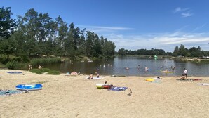 A beach with a sandy shore, a calm lake, and several people swimming and sunbathing.