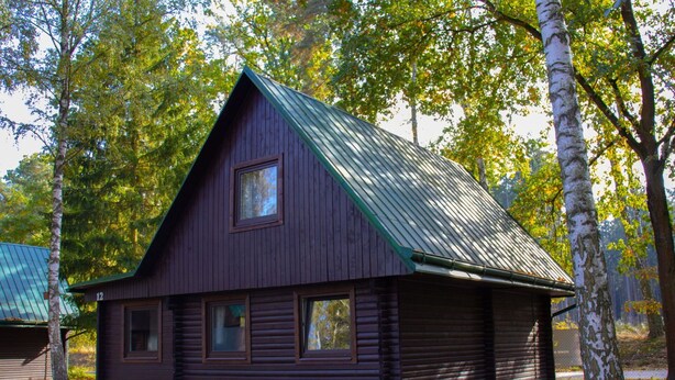 A wooden cabin with a green roof, surrounded by trees.