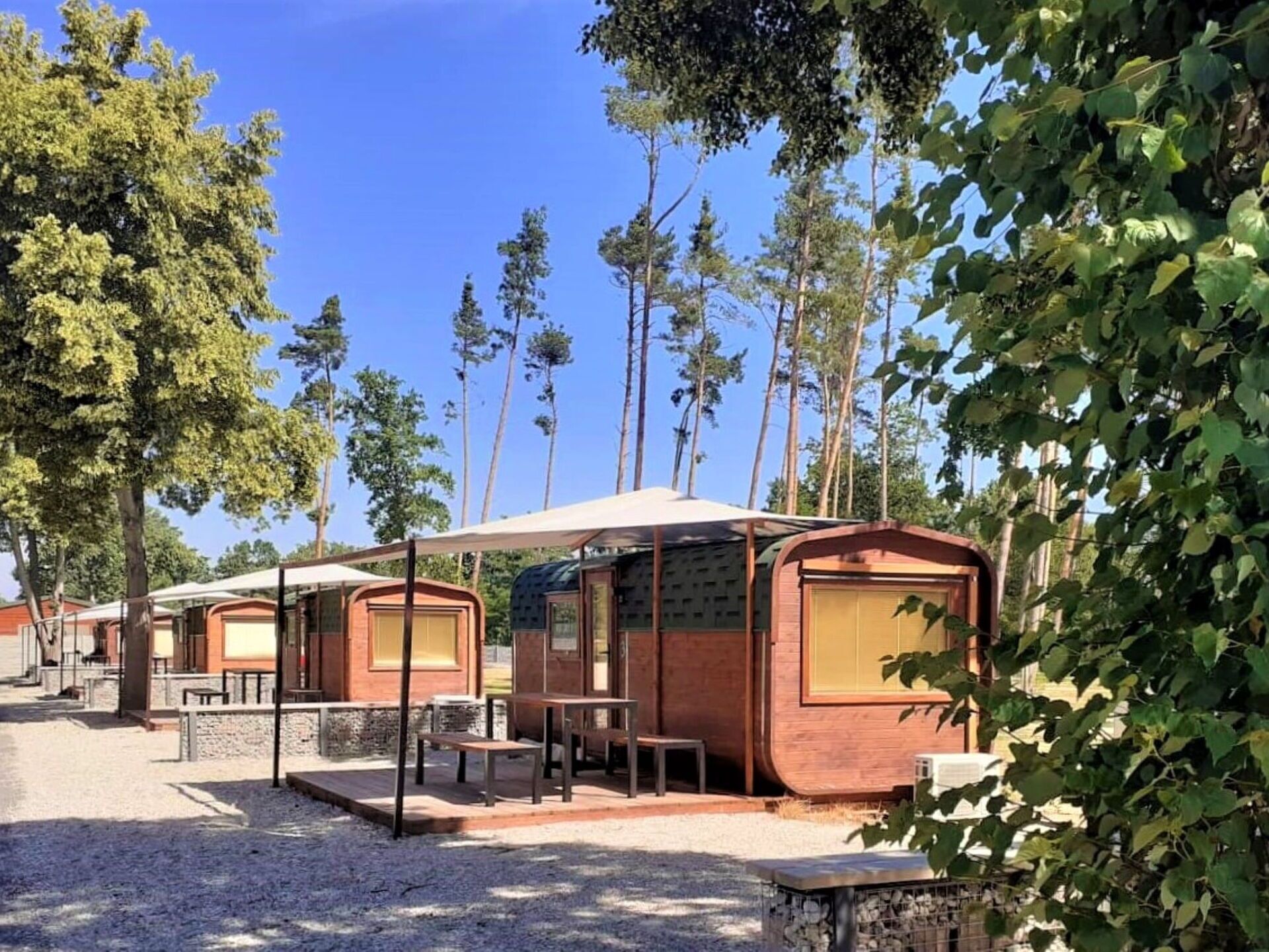 A row of wooden cabins with large windows, outdoor seating, and a gravel ground.