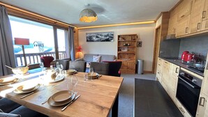 Eine moderne Küche mit Holzausstattung, ein Essbereich mit einem Holztisch, gedeckt für vier Personen, und ein Blick ins Freie durch große Fenster.