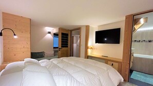 Ein Schlafzimmer mit einem großen Bett, einem an der Wand montierten Fernseher und einer Holztür.