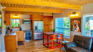 A modern kitchen with wooden cabinets, a stainless steel refrigerator, and a dining area with red chairs.