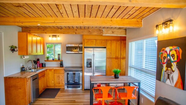 A modern kitchen with wooden cabinets, stainless steel appliances, and a dining area with orange chairs.