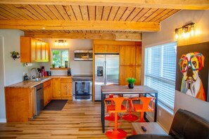 Una cocina moderna con armarios de madera, electrodomésticos de acero inoxidable y un comedor con sillas anaranjadas.