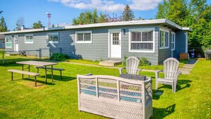 A single-story house with a front porch, a picnic table, and two Adirondack chairs.