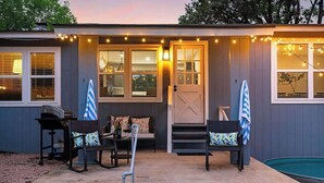 A house with a covered patio, two rocking chairs, a pool, and string lights. - Hummingbird Haus: Sleeps 12 with Hot Tub (Fredericksburg)
