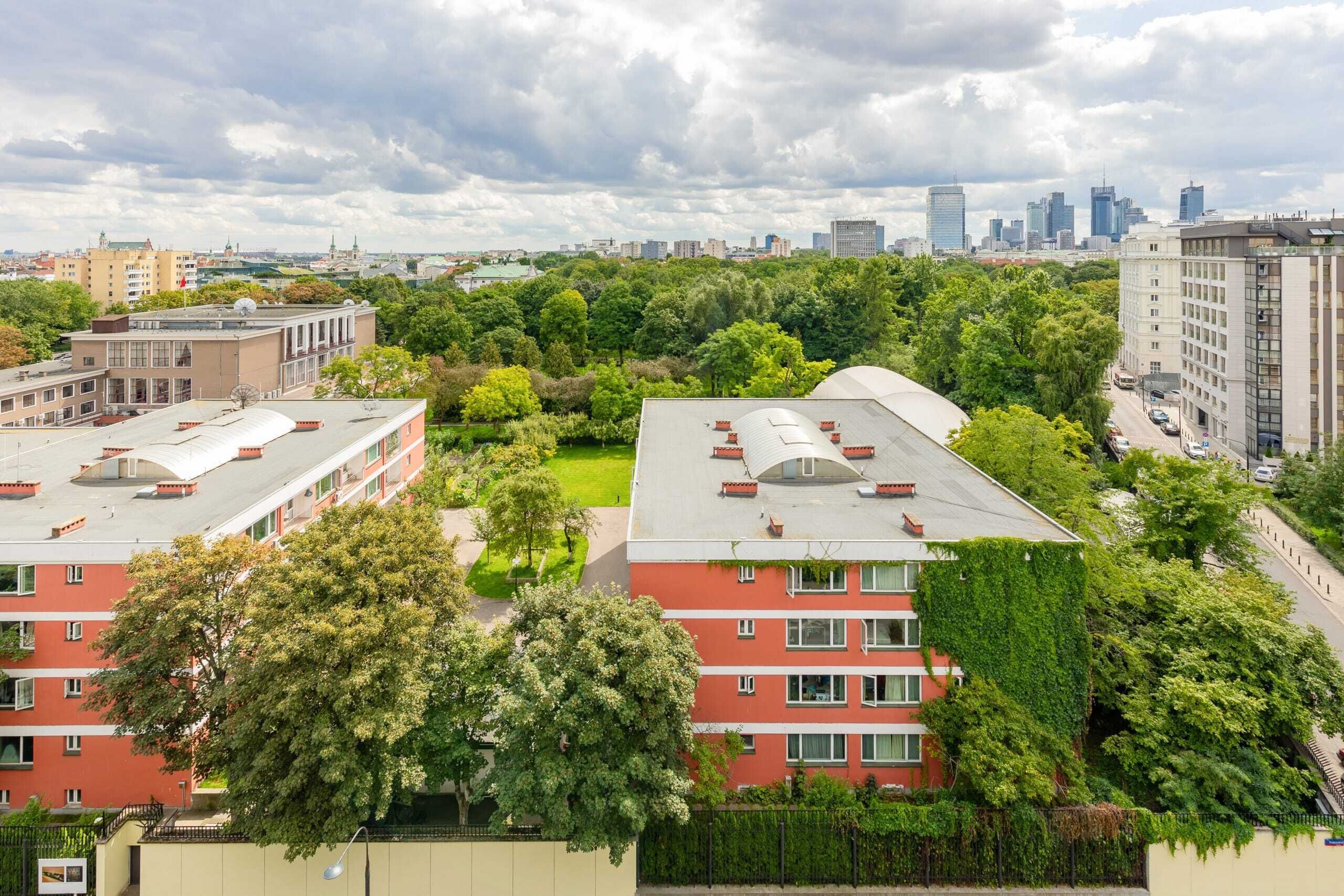 Un immeuble à plusieurs étages, doté d’une façade rouge et bordé d’arbres verdoyants au premier plan.