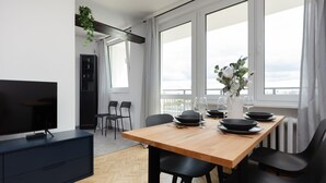 Ein moderner Essbereich mit einem Holztisch, schwarzen Stühlen und einem Fernseher auf einem dunklen Schrank.