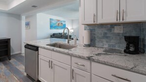 A kitchen with white cabinets, a marble countertop, a dishwasher, and a coffee maker. - Oceanfront Updated Condo - Direct Beach Access! (Satellite Beach)