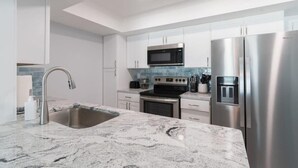 A modern kitchen with stainless steel appliances, a marble countertop, and white cabinetry. - Oceanfront Updated Condo - Direct Beach Access! (Satellite Beach)