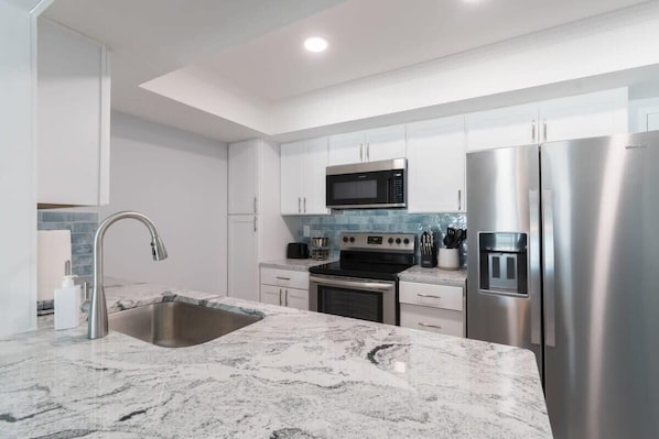 A modern kitchen with stainless steel appliances, white cabinetry, and a marble countertop. - Oceanfront condo near beach w/ balcony (Satellite Beach)