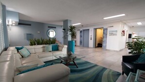 A modern living room with a beige sofa, a glass coffee table, and a blue accent wall. - Oceanfront Updated Condo - Direct Beach Access! (Satellite Beach)