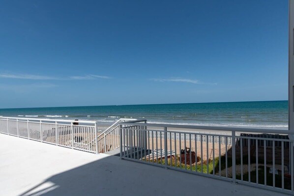 A balcony with a white railing overlooking a beach. - Oceanfront condo near beach w/ balcony (Satellite Beach)