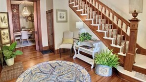 A spacious living room with a wooden staircase, a round patterned rug, and potted plants. - Spa Tub, Historic B & B, Get Spoiled! (Eureka Springs)