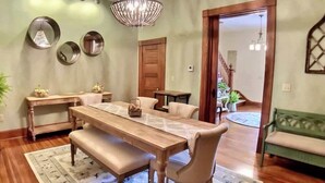 Un coin repas avec une table en bois, des bancs et un lustre. On y trouve deux petites tables d’appoint avec des paniers, et un miroir est accroché au mur.