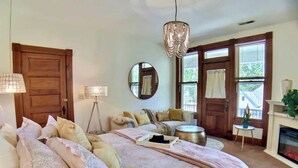 A bedroom with a large bed, a round mirror, a chandelier, a fireplace, and a window with curtains. - 2 Bedroom Suite in Historic B&B, Breakfast Include (Eureka Springs)