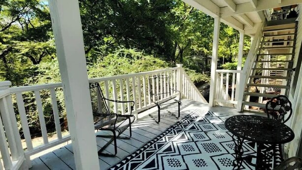 Une véranda couverte avec une table et des chaises en métal noir, entourée de balustrades blanches et dotée d’un sol à motifs.