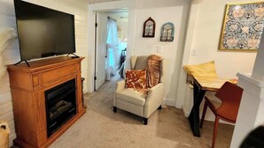 Un salon avec une cheminée, un téléviseur, un fauteuil orné d’un coussin à motifs et une table avec un coussin jaune.