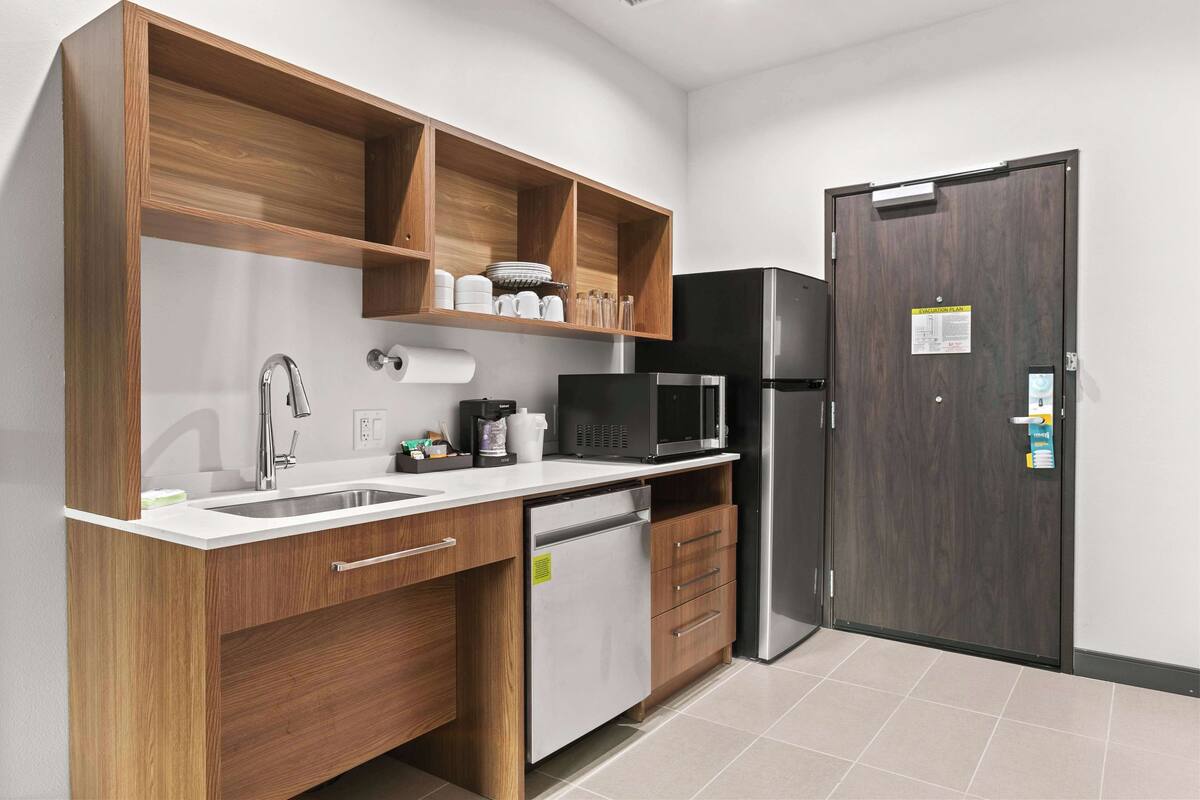 A modern kitchen with wooden cabinets, a stainless steel refrigerator, a microwave, and a dishwasher.