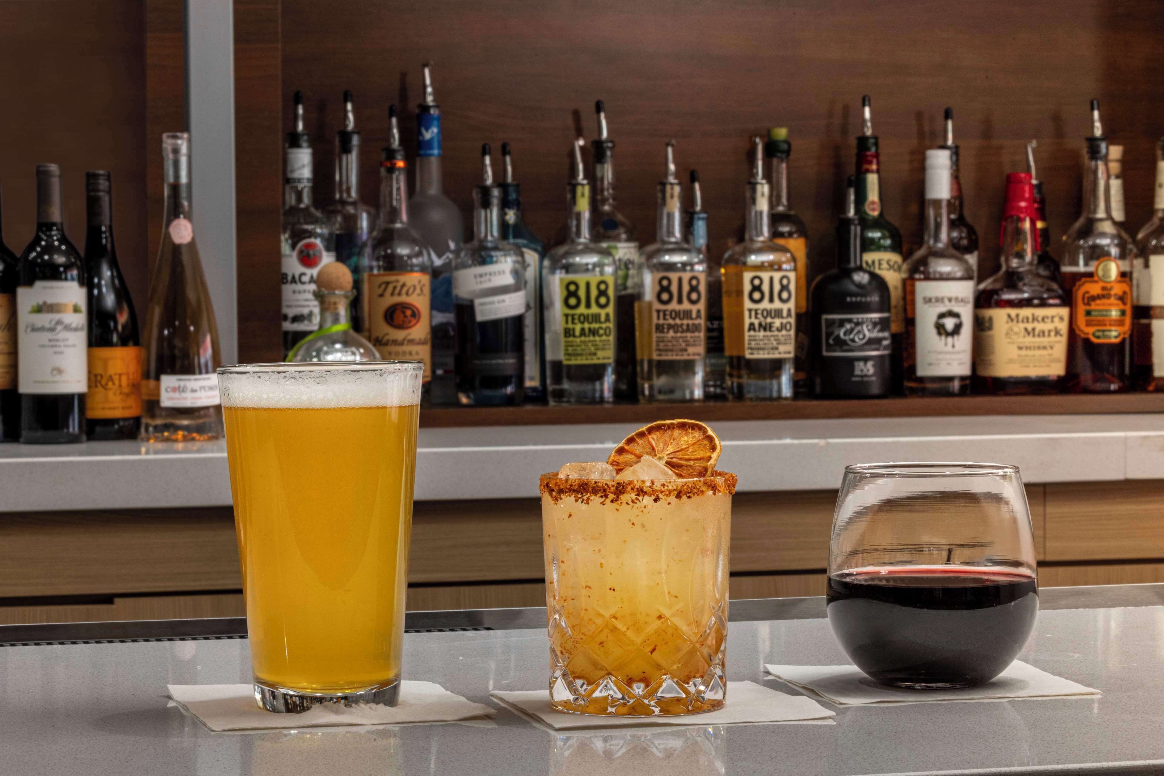 Un bar con varias botellas de licores y tres vasos de diferentes bebidas.
