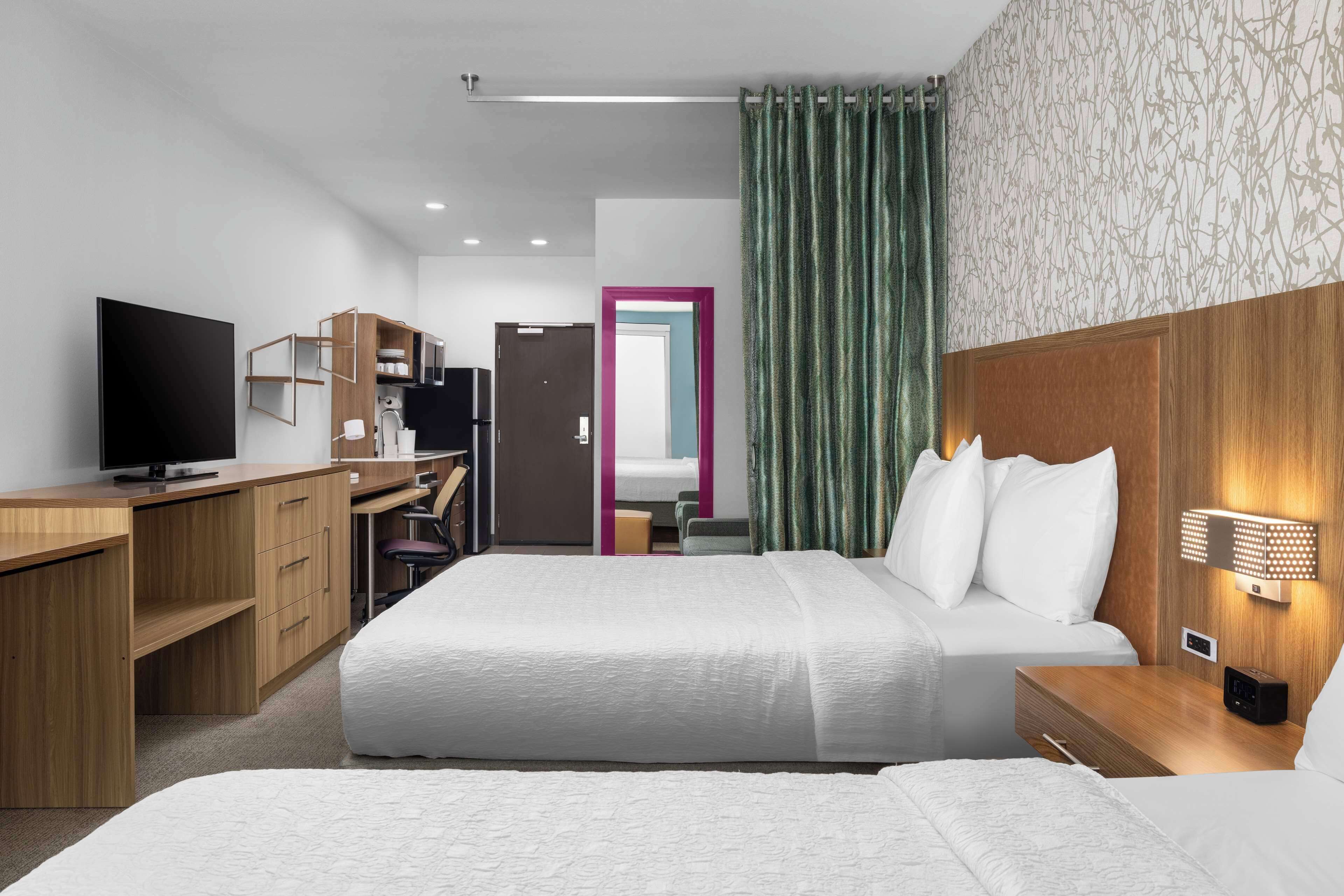 A hotel room with a bed, bedside table, TV, desk, and wardrobe.