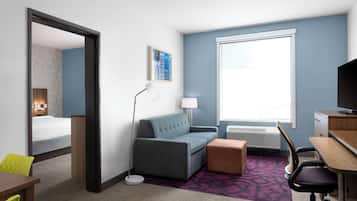 Habitación de hotel con cama, sofá, escritorio, silla, lámpara, televisión y ventana.