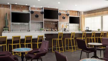 A bar area with a brick wall, shelves with bottles, and yellow chairs.