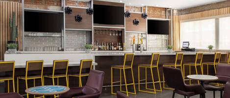 A bar area with a brick wall, shelves with bottles, and yellow chairs.