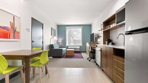 A modern kitchen with a built-in refrigerator, a dining area with a wooden table and bright green chairs, and a cozy seating area with a gray sofa and a small ottoman.