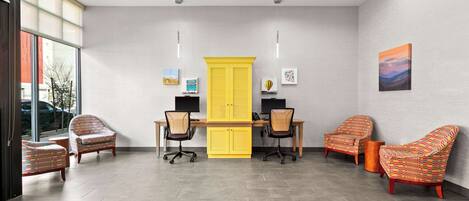 A modern office space with a desk, two chairs, a yellow cabinet, and artwork on the walls.