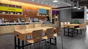 A modern restaurant with wooden tables and chairs, a brick wall, and a counter with various food items.