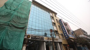 A building with a glass facade and multiple signs, including 'DISCOVER FASHIONS INDIA LTD' and 'AARYAN FAB'. - Hotel Raaso Inn Tuglkabad (New Delhi)