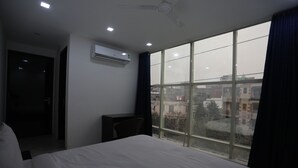 A hotel room with a large bed, a desk, and a window with a view of buildings. - Hotel Raaso Inn Tuglkabad (New Delhi)