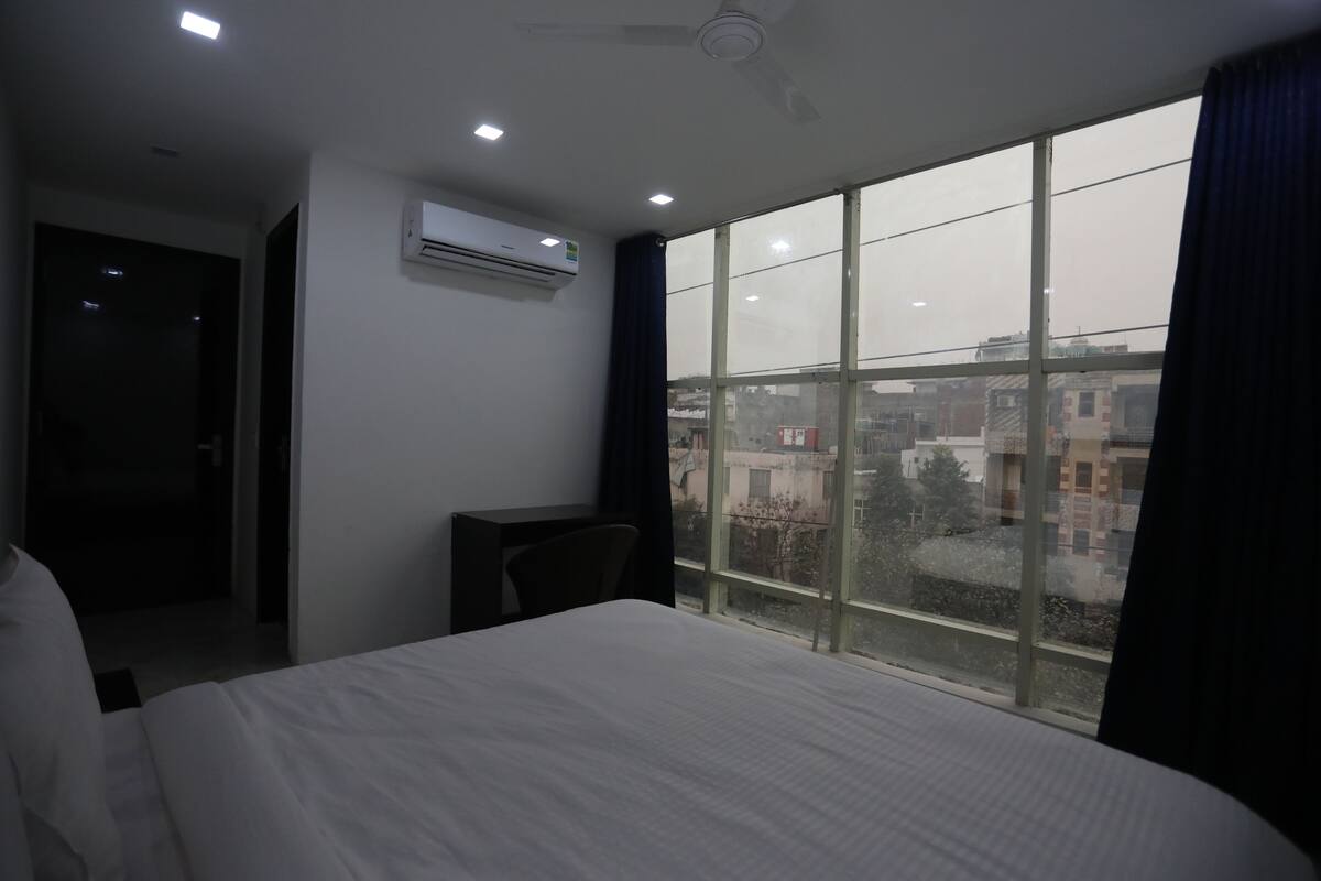 A hotel room with a large bed, a desk, and a window with a view of buildings.