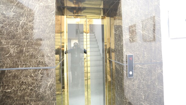An elevator with a marble wall and a glass door. - Hotel Raaso Inn Tuglkabad (New Delhi)