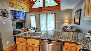 A kitchen with granite countertops, wooden cabinets, a dishwasher, and a stone fireplace.