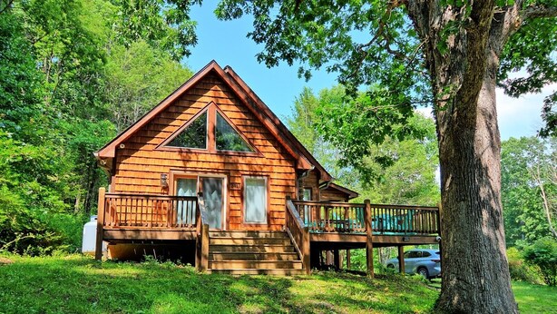 A wooden cabin with a porch and a deck, surrounded by trees.