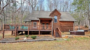 A wooden cabin with a deck, a hot tub, and a stone pathway leading to the entrance.