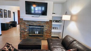 A living room with a stone fireplace, a large flat-screen TV, a leather sofa, and a lamp.