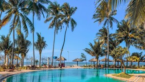 A pool surrounded by palm trees and beach umbrellas, with a clear view of the ocean. - TENT GLAMPING -MUINE SUN & SEA  (Mui Ne)