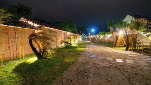 A nighttime view of a resort with a paved pathway, tents, and a brick wall. - TENT GLAMPING -MUINE SUN & SEA  (Mui Ne)