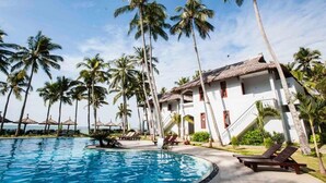 A resort with a swimming pool, palm trees, and a building with a thatched roof. - TENT GLAMPING -MUINE SUN & SEA  (Mui Ne)