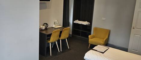 A hotel room with a bed, a desk with chairs, a television, and a wardrobe.