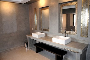 A modern bathroom with two white sinks, a bench, and large mirrors with decorative frames.