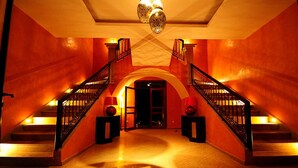 A grand staircase with ornate railings and a chandelier, leading to a dark doorway. - VICTOR HOME RENT (Jbilate)