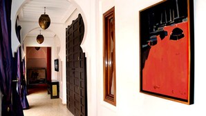 A hallway with a dark wooden door, a framed abstract painting, and a hanging light fixture. - VICTOR HOME RENT (Jbilate)