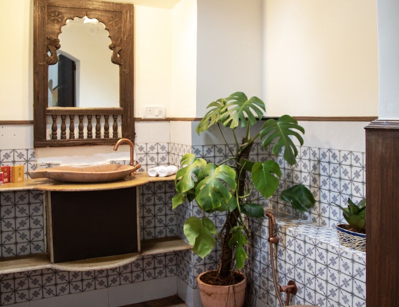 Een badkamer met een houten wastafel, een spiegel met decoratieve lijst, betegelde wanden en een potplant.