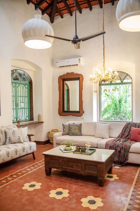 A living room with a sofa, coffee table, and decorative items. There is a window with a view of greenery and a mirror on the wall.
